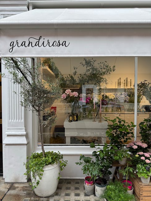 The image shows the exterior of a flower shop named 'grandirosa,' with a large glass window displaying an interior filled with various floral arrangements and vases. In front of the shop, there is a w